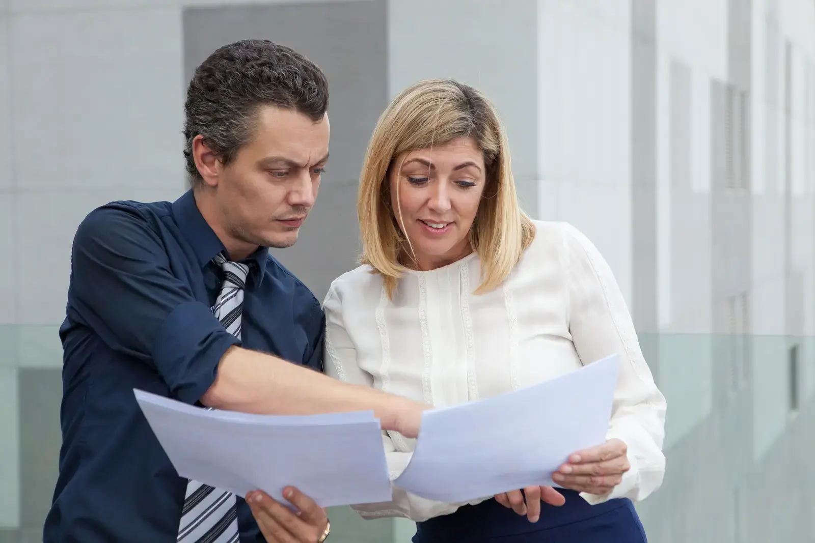 Two colleagues reading through printed documents together outside an office building